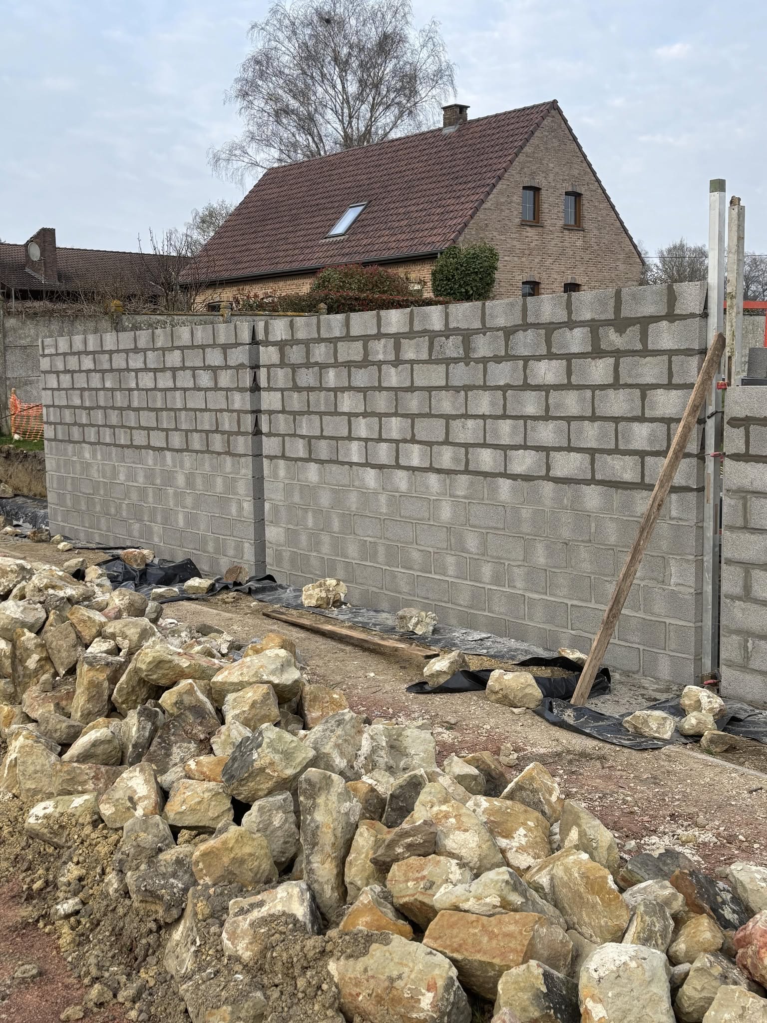 Mur en blocs béton en cours avec terrain décaisse et pierres au sol